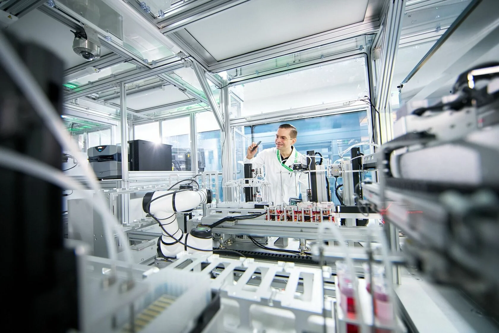 Researcher in a white lab coat working beside robotic laboratory equipment