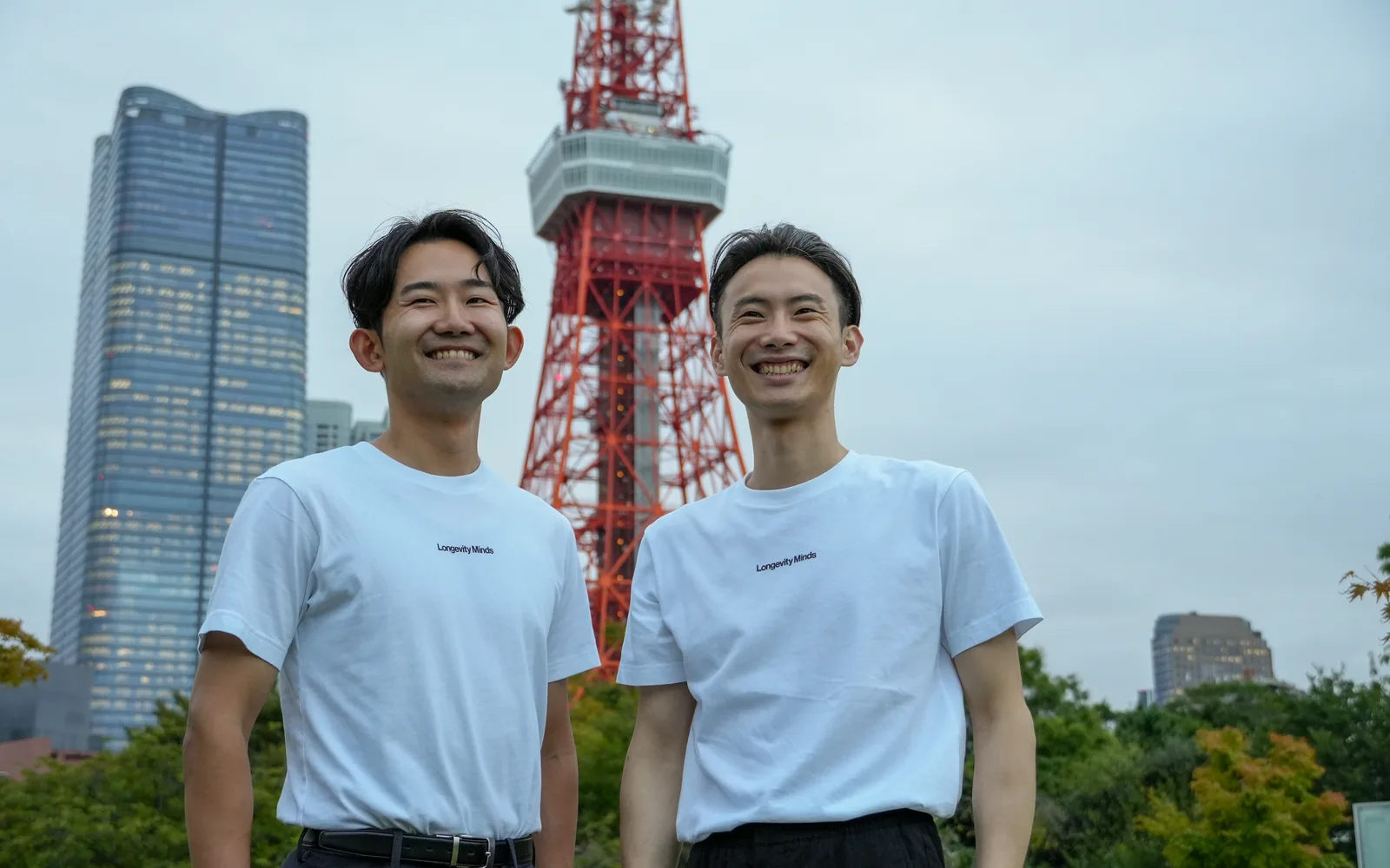 Two men in white Longevity Minds T-shirts stand in front of Tokyo Tower